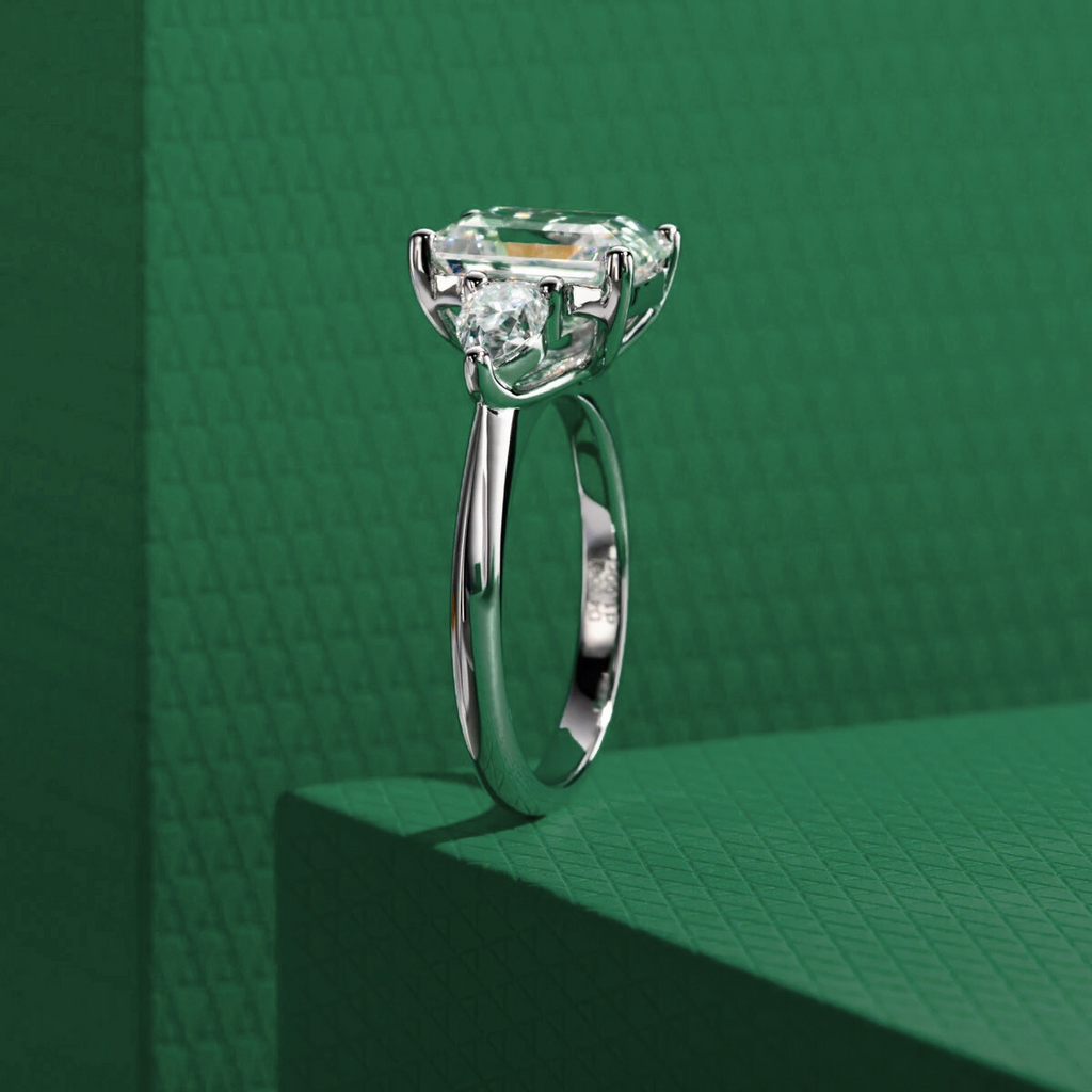 Anel solitário em prata com pedra central esmeralda e moissanite sobre fundo verde texturizado