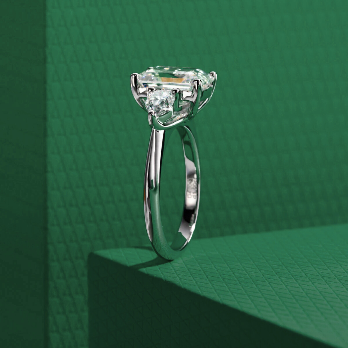 Anel solitário em prata com pedra central esmeralda e moissanite sobre fundo verde texturizado