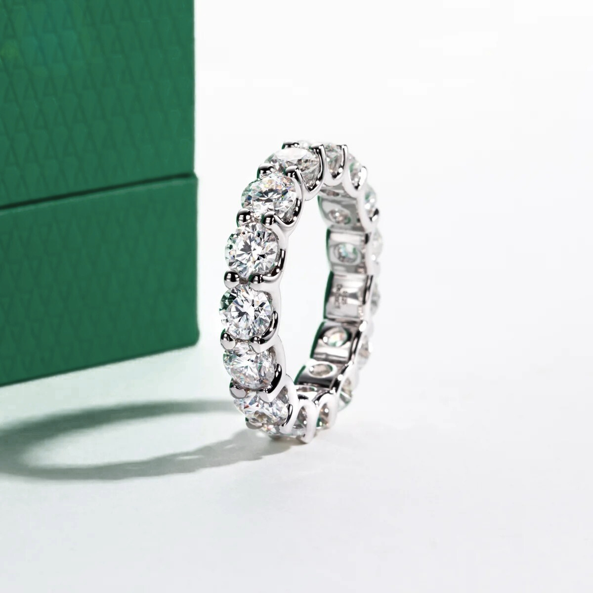 Aliança de prata com brilhantes moissanite redondos, ao lado de caixa verde texturizada