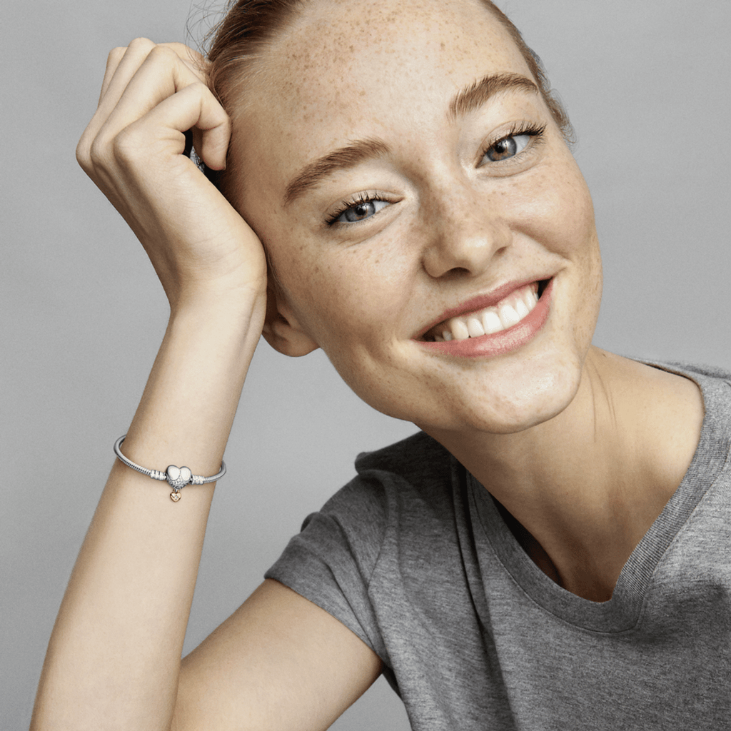 Mulher sorridente com pulseira de prata com pingente de coração em fundo cinza