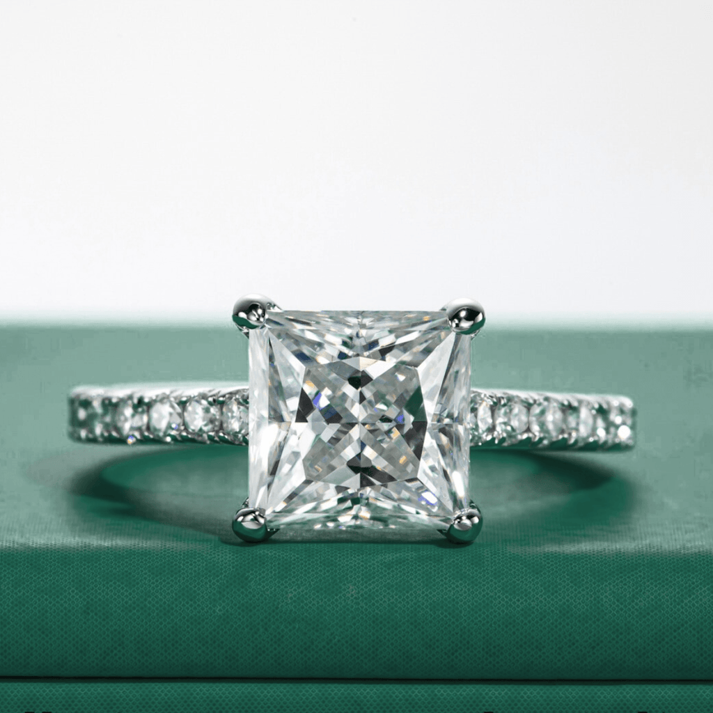 Anel solitário de moissanite princesa com pedras laterais cravejadas em fundo verde