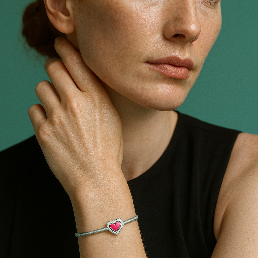 Pulseira berloque em prata 925 com coração rosa vibrante no pulso de mulher com roupa preta